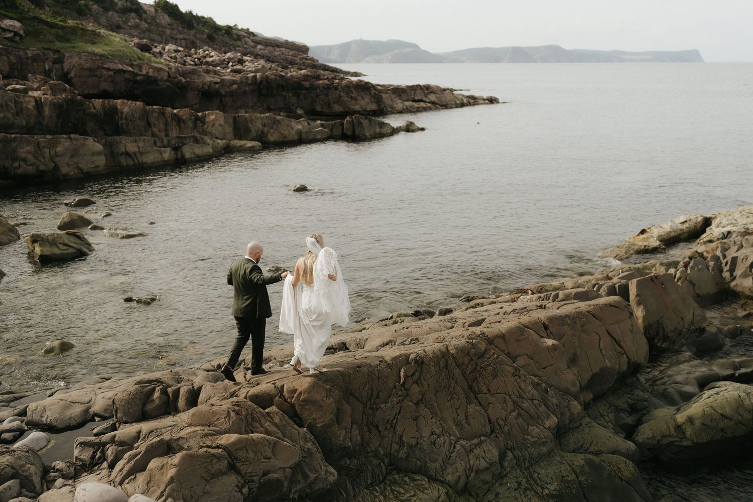 A rocky coastline with water and misty mountains in the distance creates a dramatic coastal landscape.