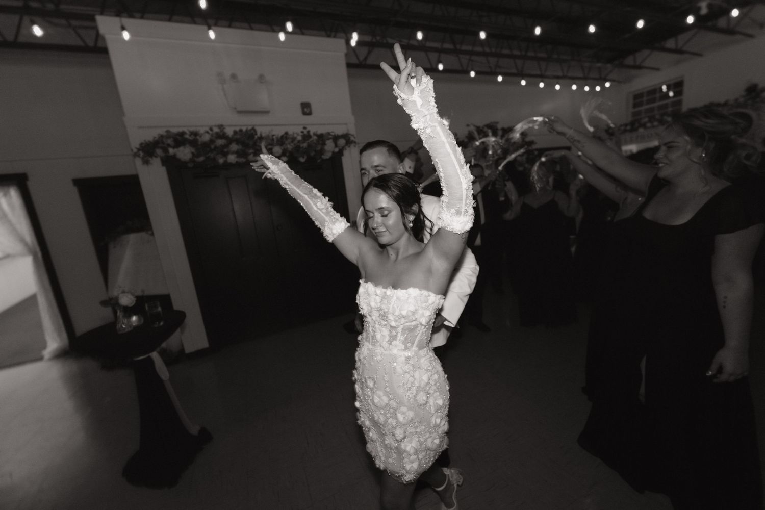 Dancers perform at a dimly lit reception venue with string lights hanging overhead creating a romantic atmosphere.
