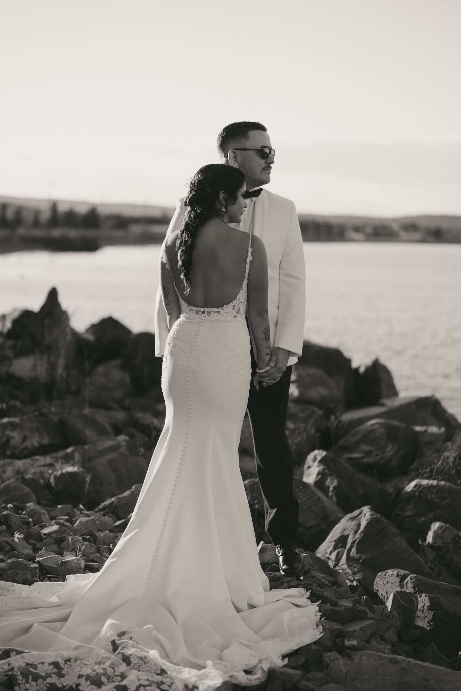 A couple in wedding attire poses on black volcanic rocks near the ocean in a series of black and white photographs.