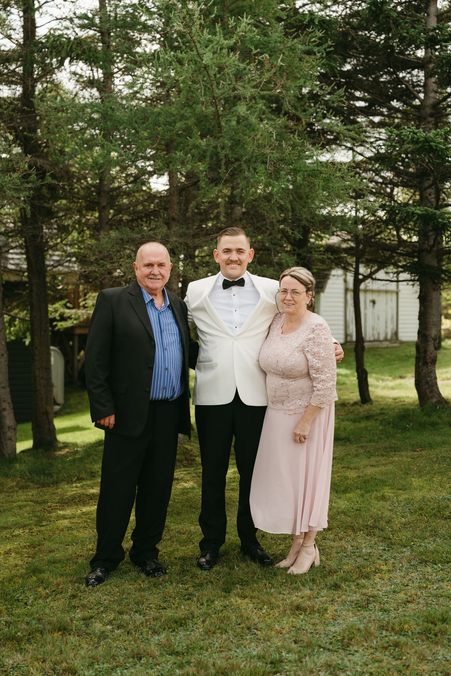 A group stands outdoors on grass in formal attire with trees in the background.
