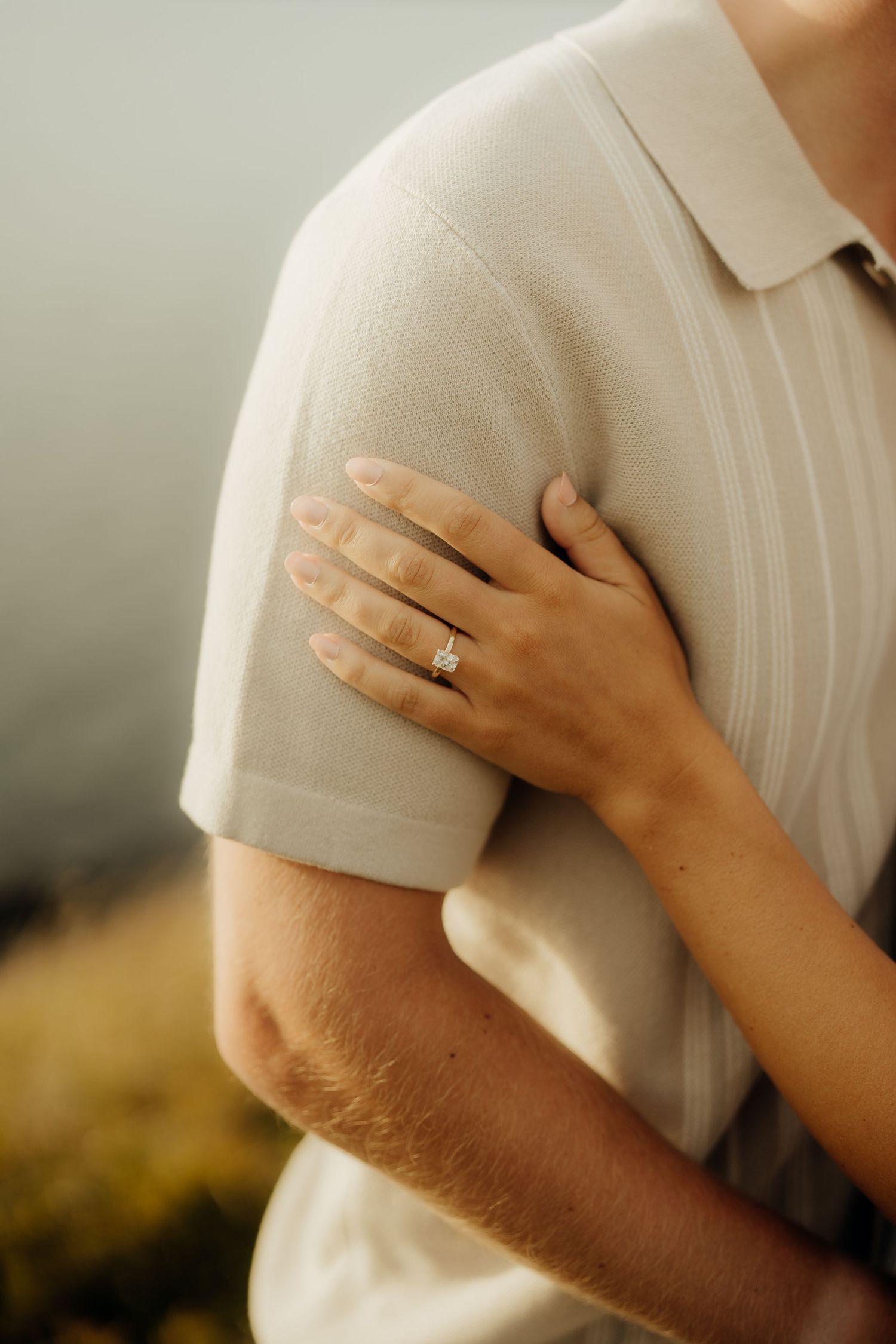 Close-up view of hands holding each other tenderly against a white shirt with a blurred background.