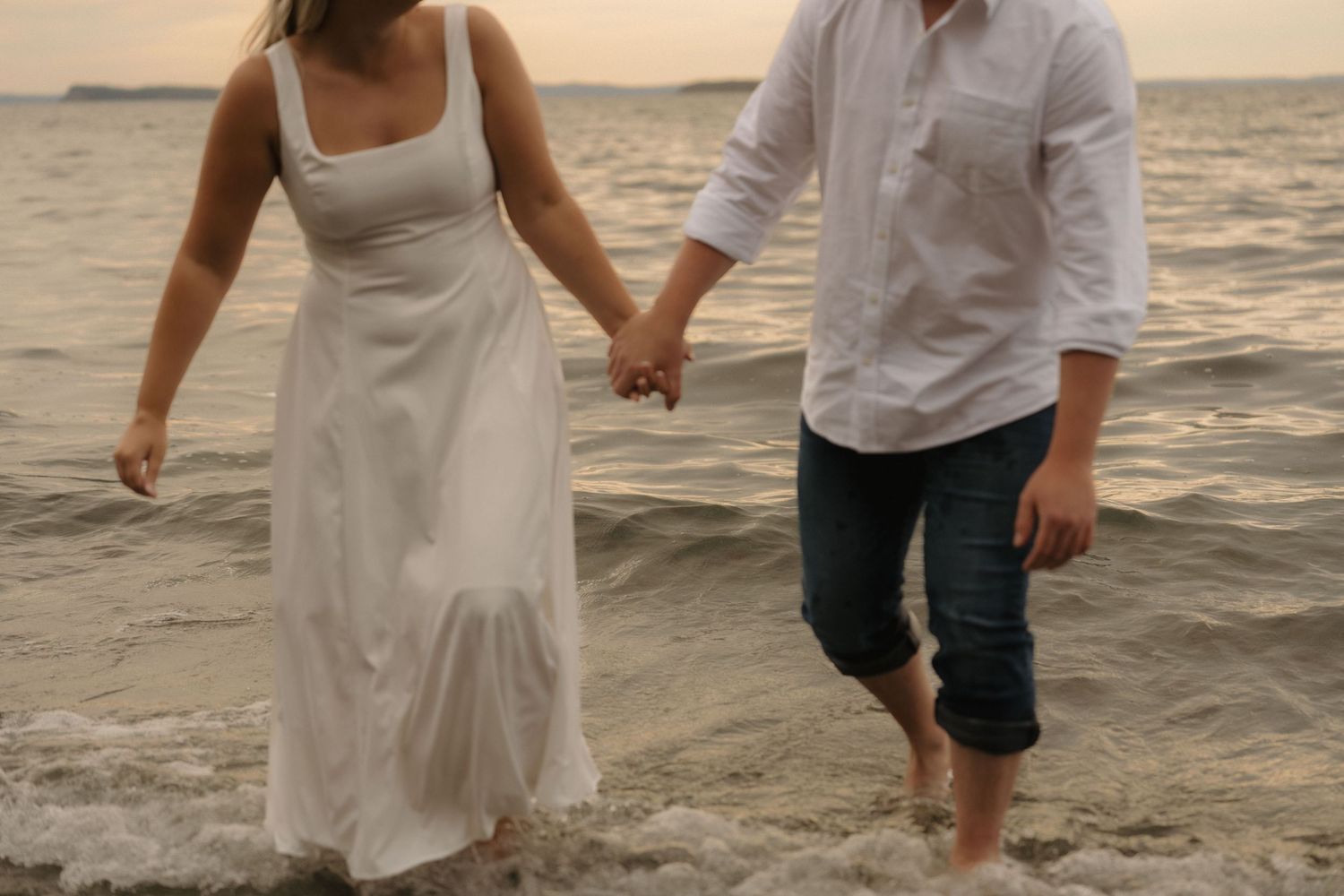 Couple strolling together on sandy beach during golden hour with ocean waves in background.
