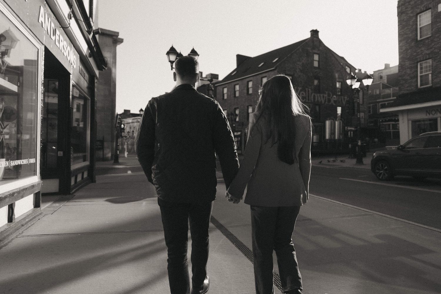 Black and white photo of a couple holding hands while walking down a charming urban street.