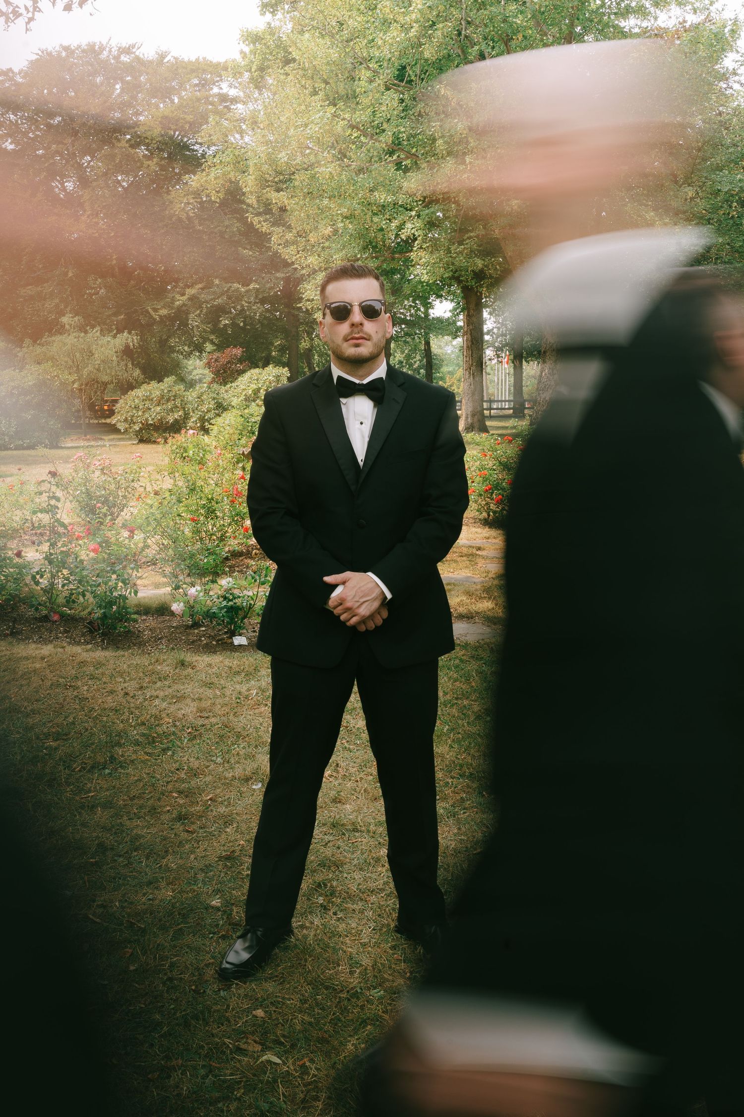 Groomsmen in sunglasses and tuxedos posing casually outdoors.