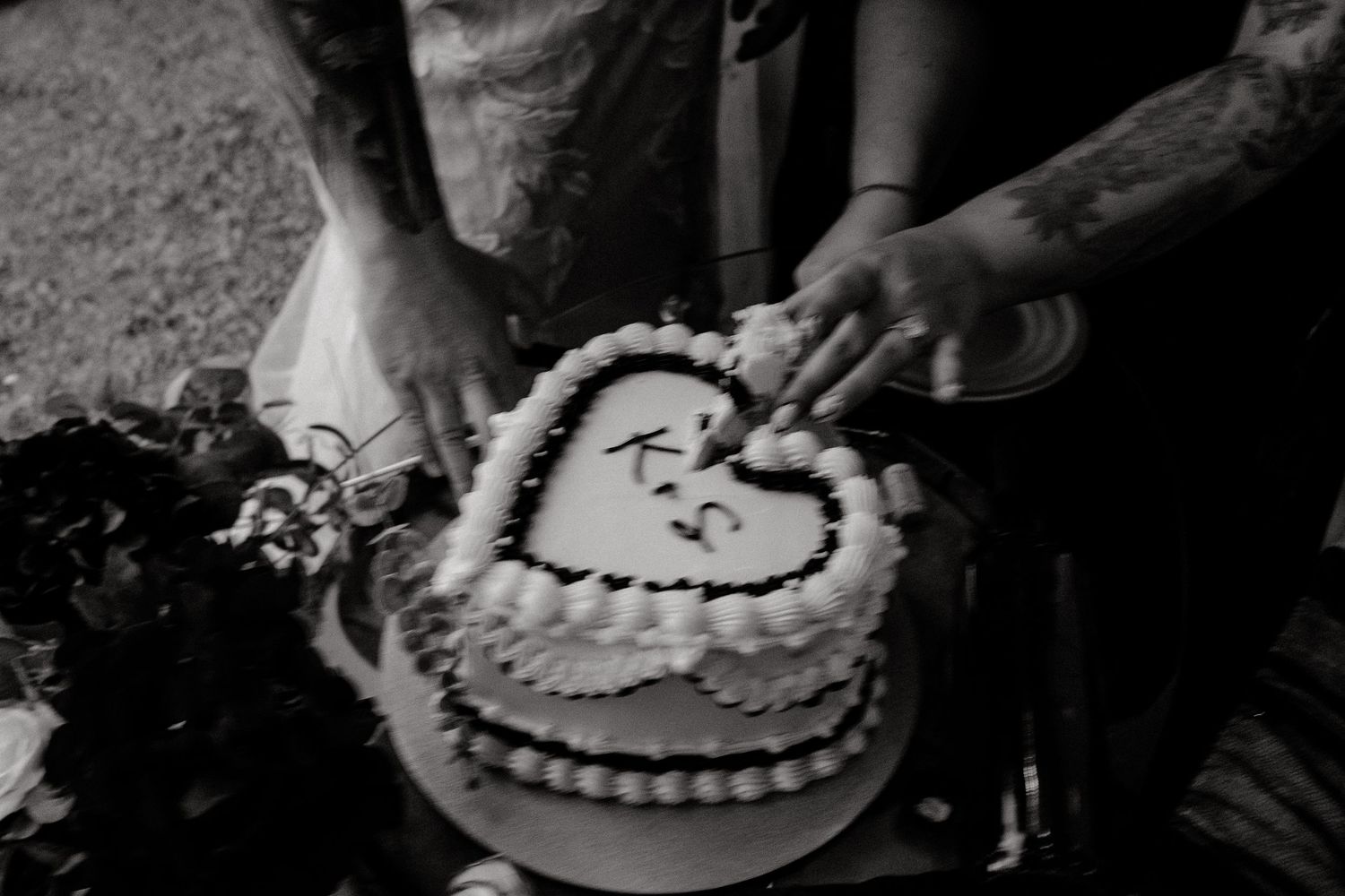 Black and white close-up of hands cutting heart-shaped wedding cake.