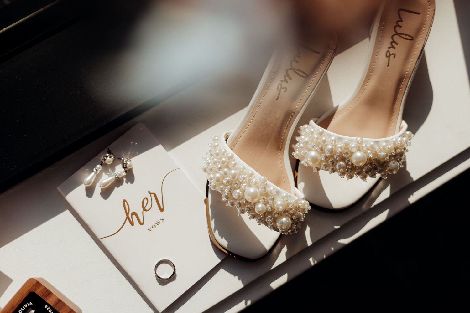 Wedding shoes and invitation details arranged in dramatic lighting with shadows.