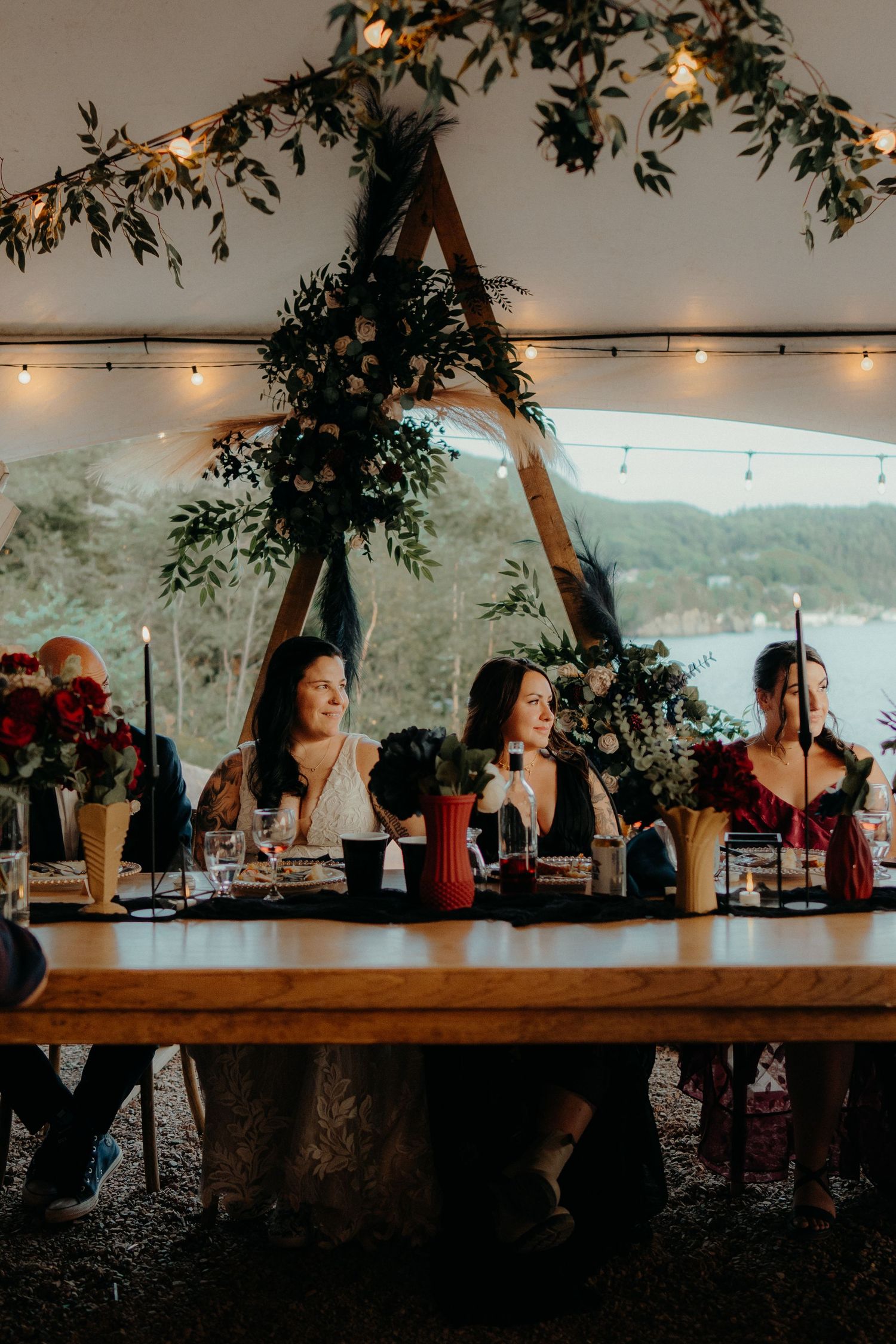 Reception dinner setup under tent with greenery arch and string lights.