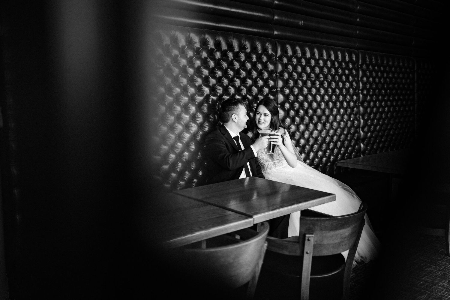Romantic couple seated at dimly lit bar with geometric wall pattern behind them.