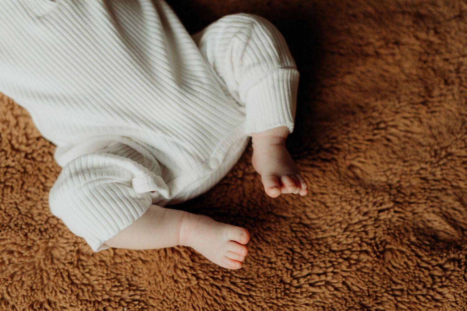 Sleeping infant in white ribbed sweater lying on soft brown carpet.