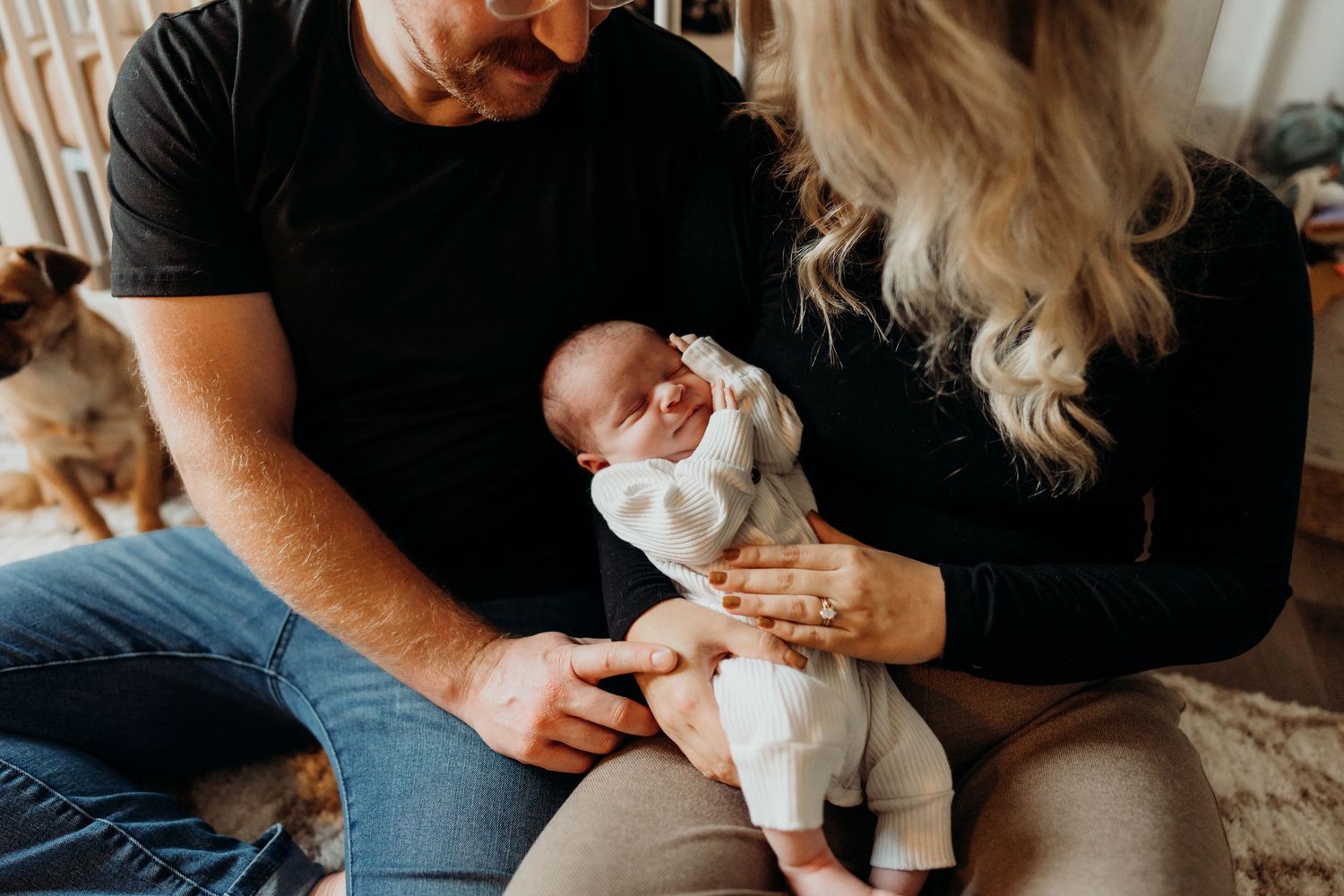 Candid indoor shot of a baby wearing white being held on a patterned carpet.