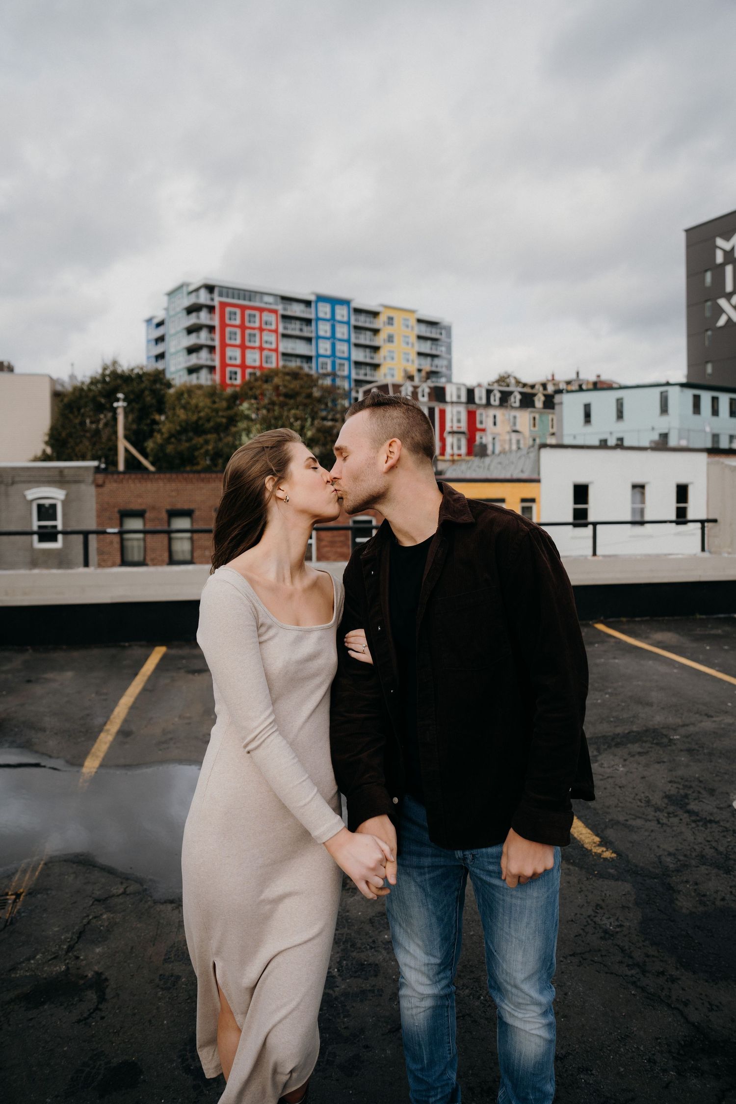 Romantic couple in casual attire shares playful moments in an urban rooftop parking area.