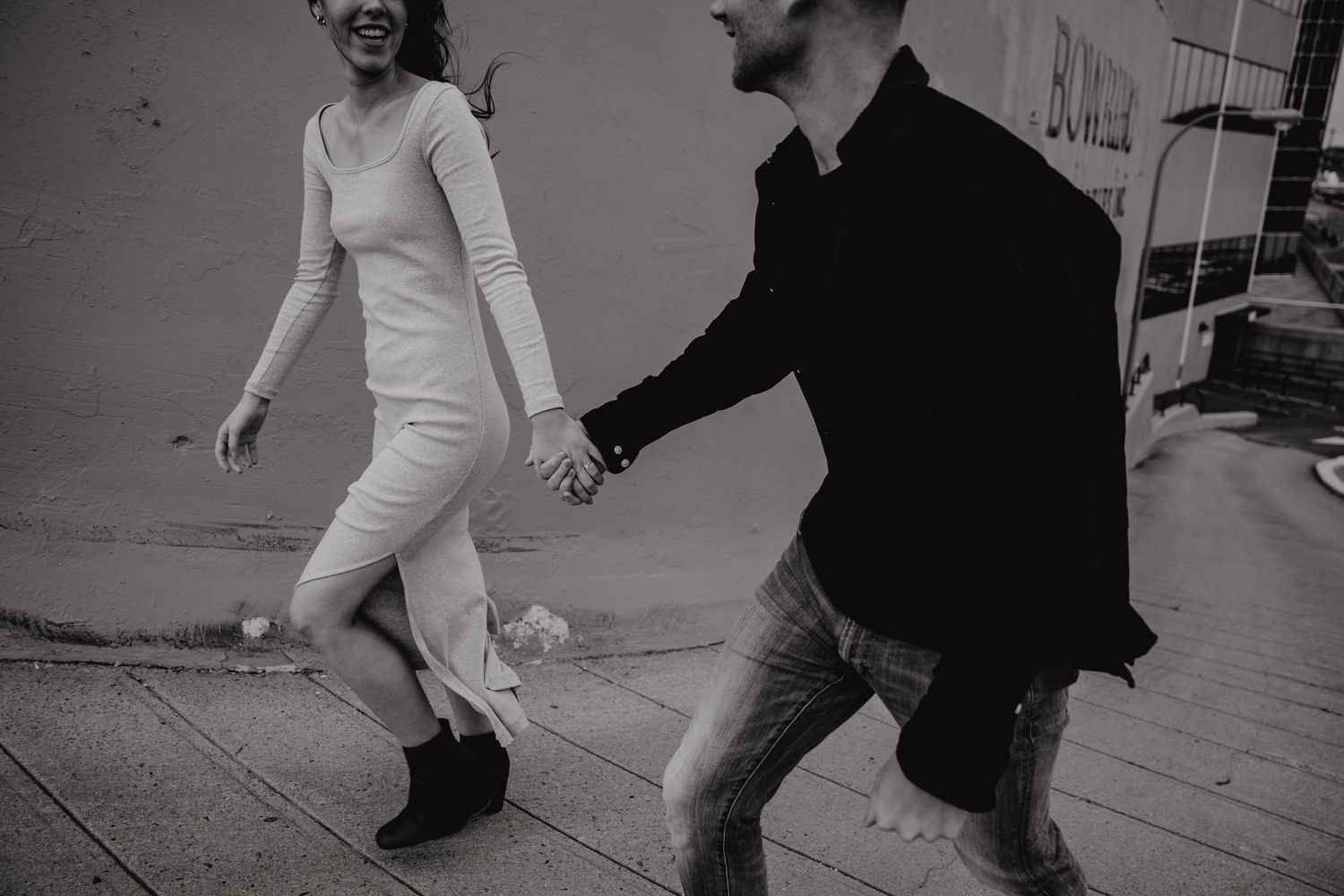 Black and white photo of two people in a playful pose against an urban wall.