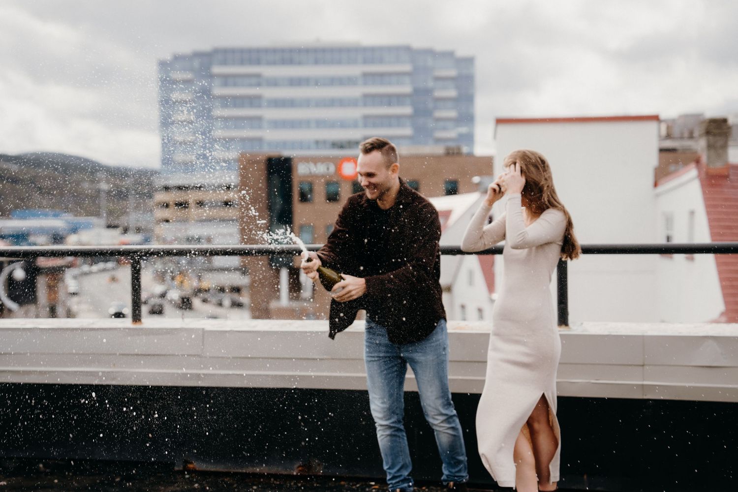 Two people embrace during what appears to be a proposal on a city rooftop.