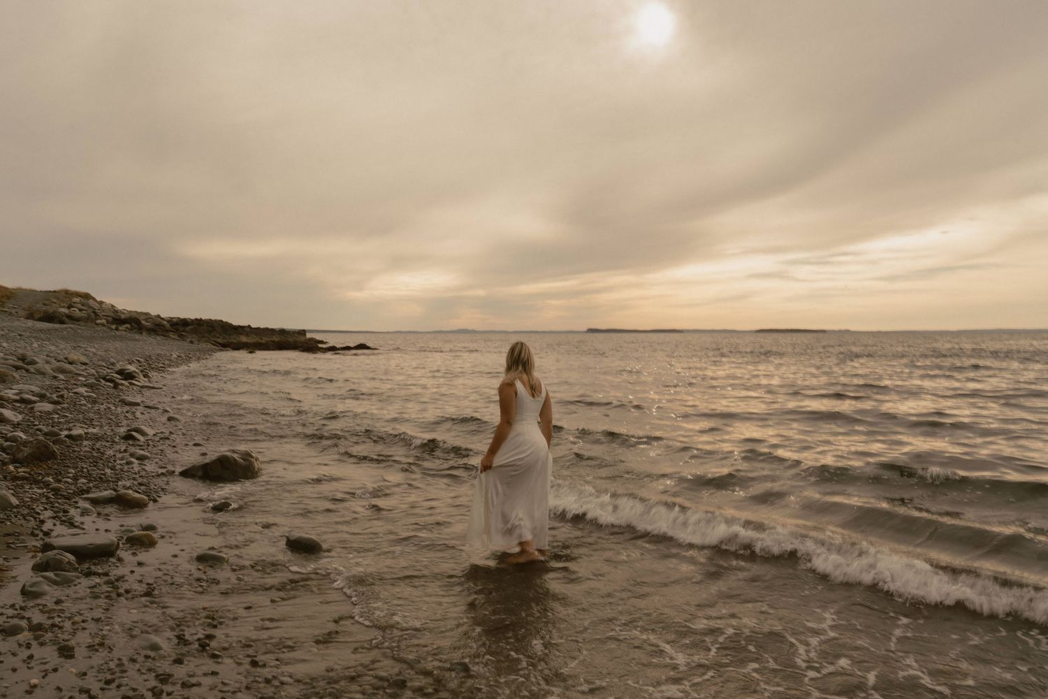 Silhouette of a person in white dress dancing by the ocean waves during golden hour.