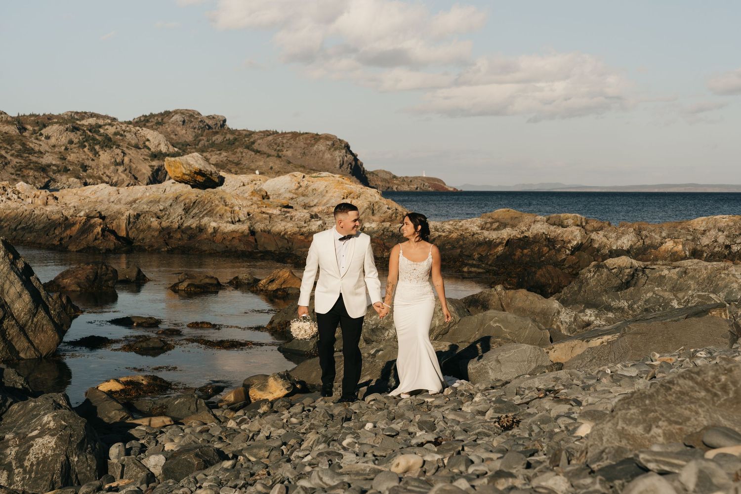 A couple shares a romantic moment on rugged coastal cliffs overlooking the ocean at sunset.