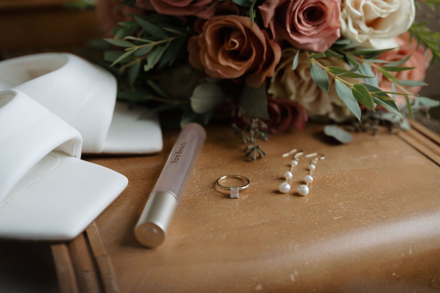 Elegant wedding details including pink and cream roses, rings, and invitations arranged on a wooden surface.