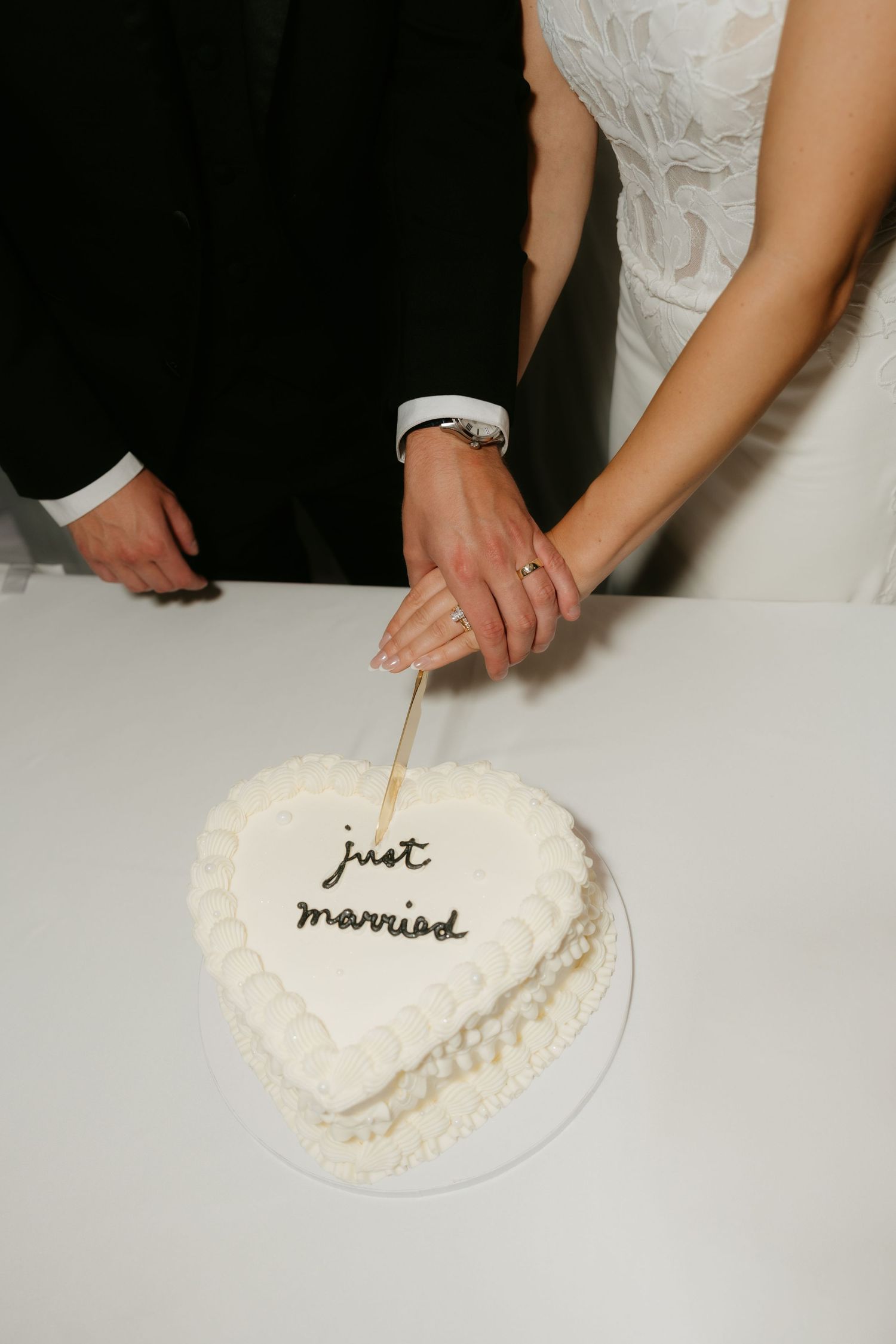 Bride and groom cutting a heart-shaped white wedding cake inscribed with just married in cursive frosting.