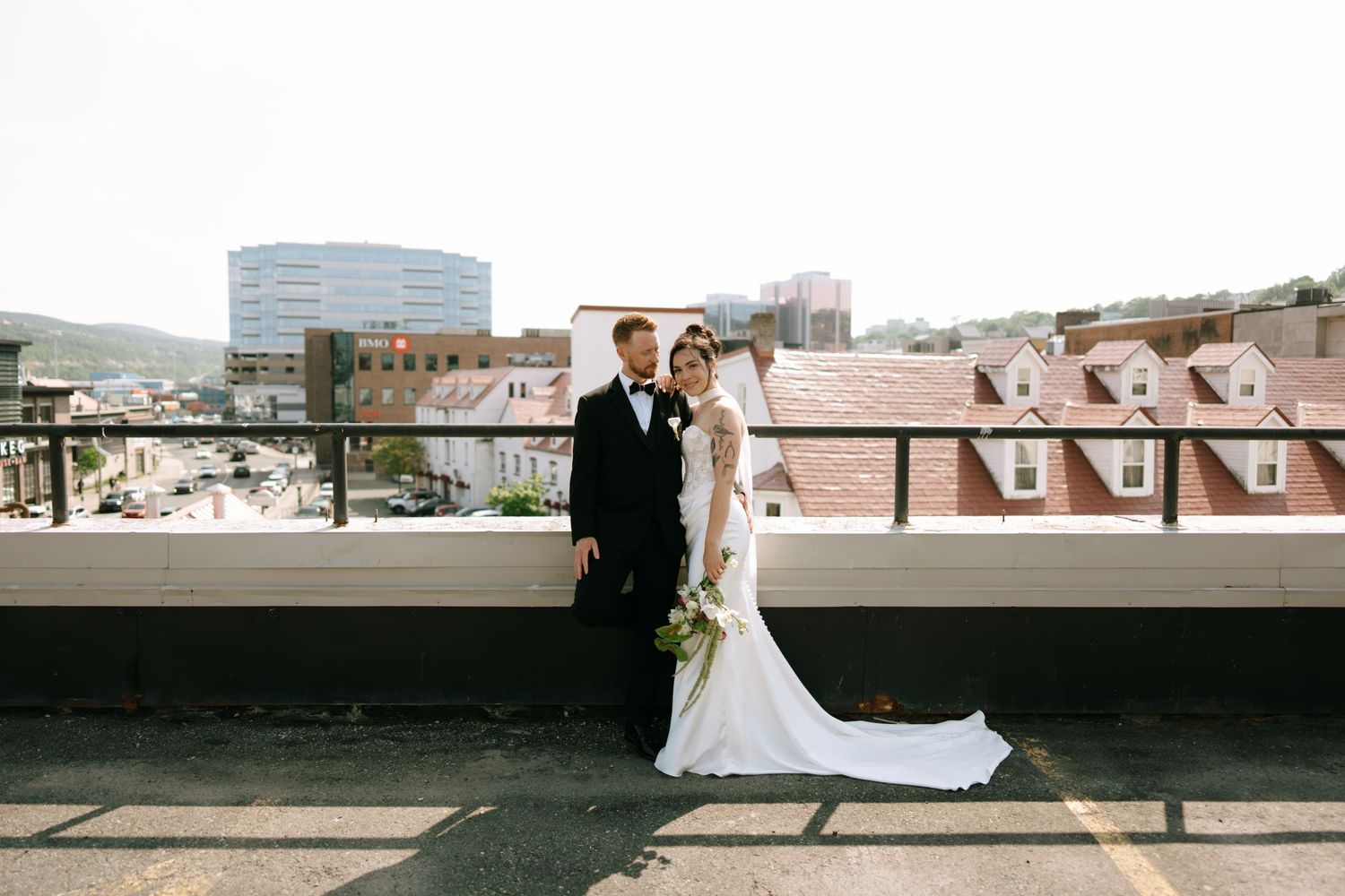 Bride and groom pose on rooftop venue with city skyline backdrop on their wedding day.