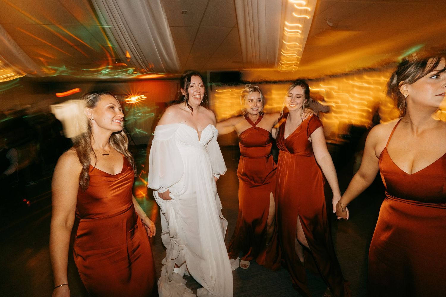 Guests dancing and celebrating at a wedding reception with warm amber lighting and burgundy bridesmaid dresses.