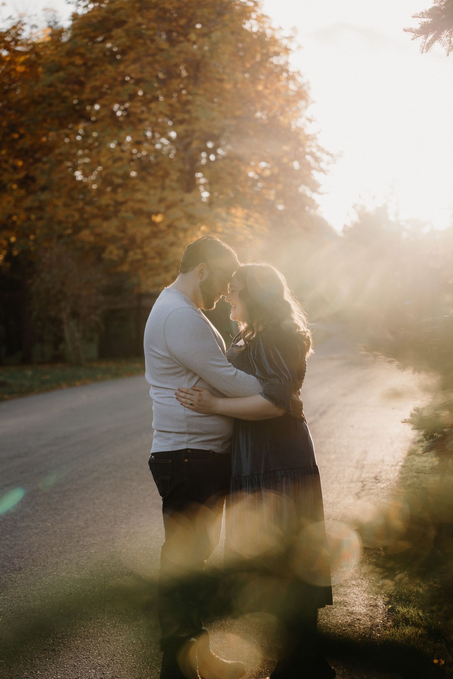A loving couple embraces in a sunlit park during golden hour.