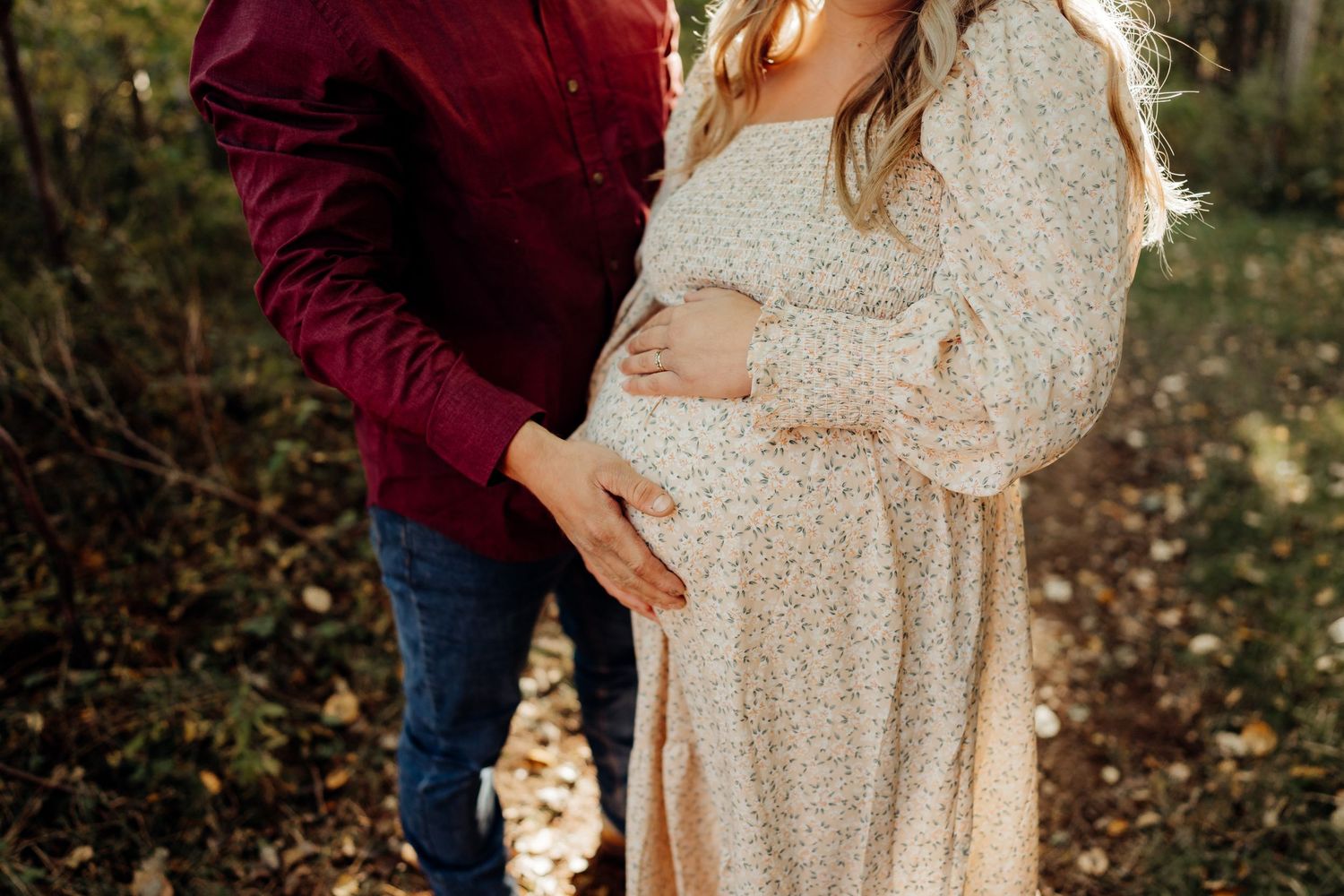 Romantic fall photoshoot in a field with burgundy and cream outfits surrounded by autumn foliage.