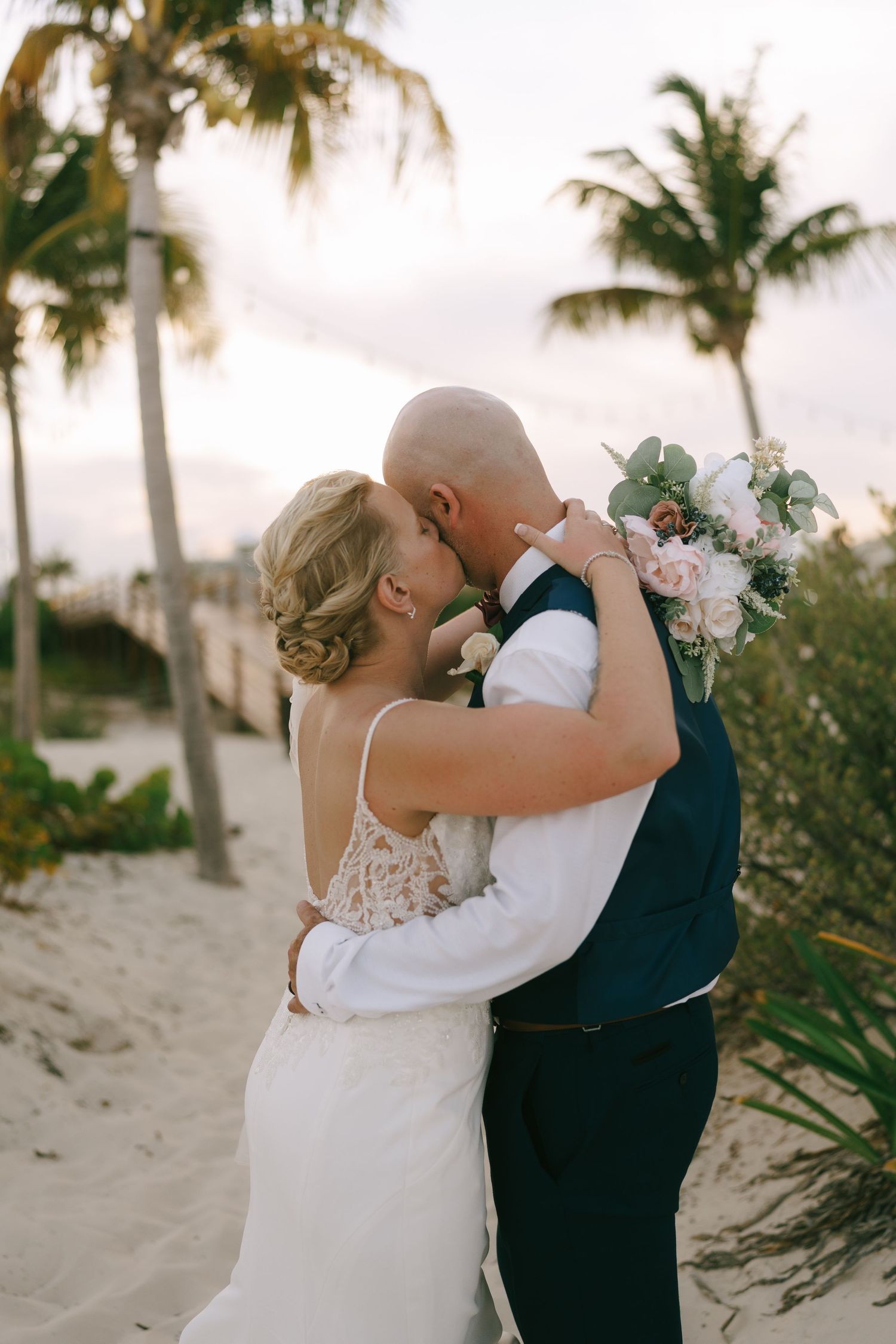 Romantic wedding moment captured on a sandy beach with swaying palm trees.