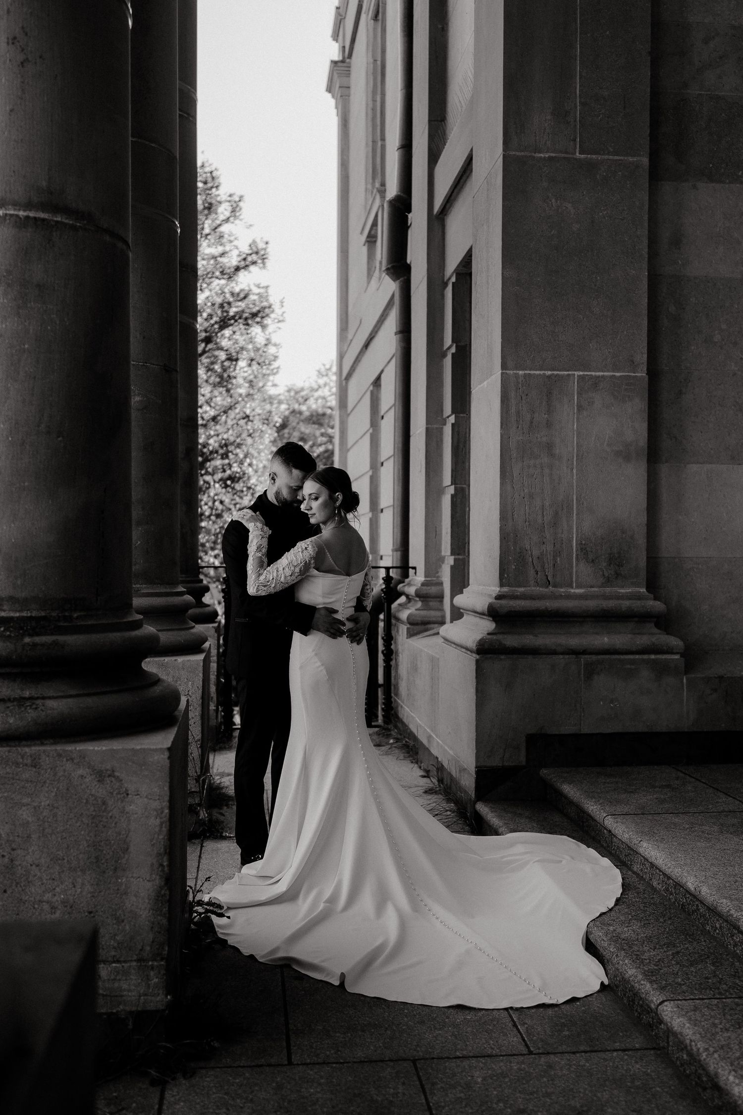 Black and white wedding portraits captured in elegant architectural setting with columns and dramatic lighting.