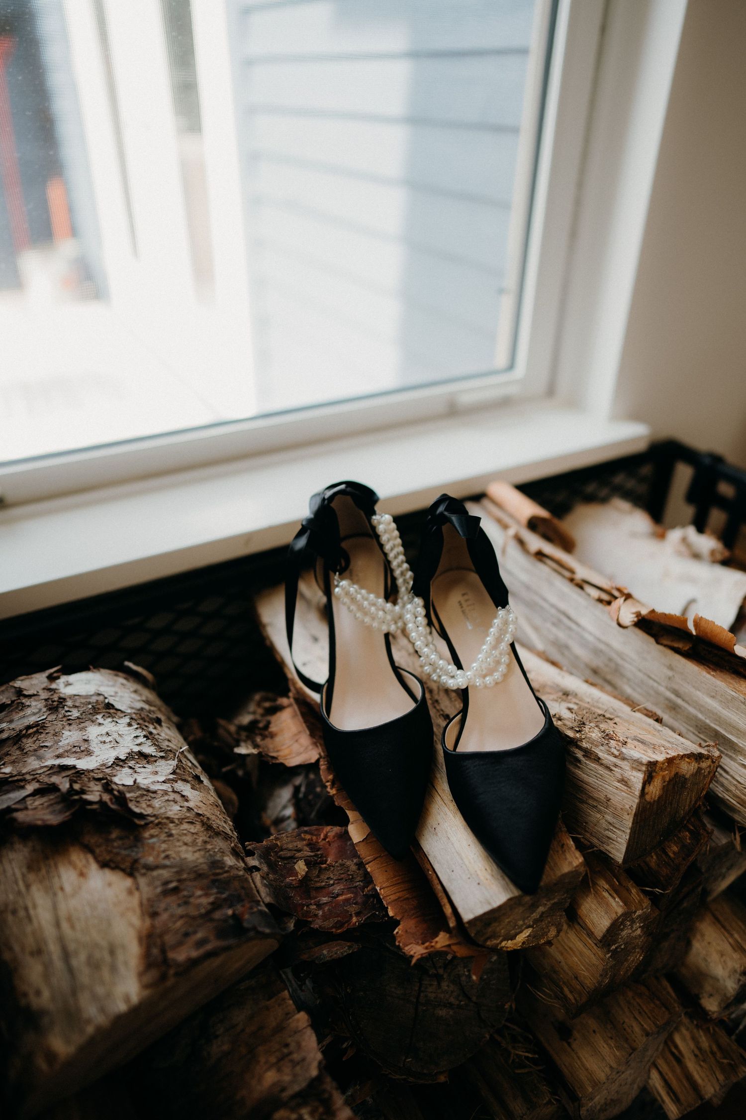 Elegant black wedding shoes displayed on rustic driftwood by a window.