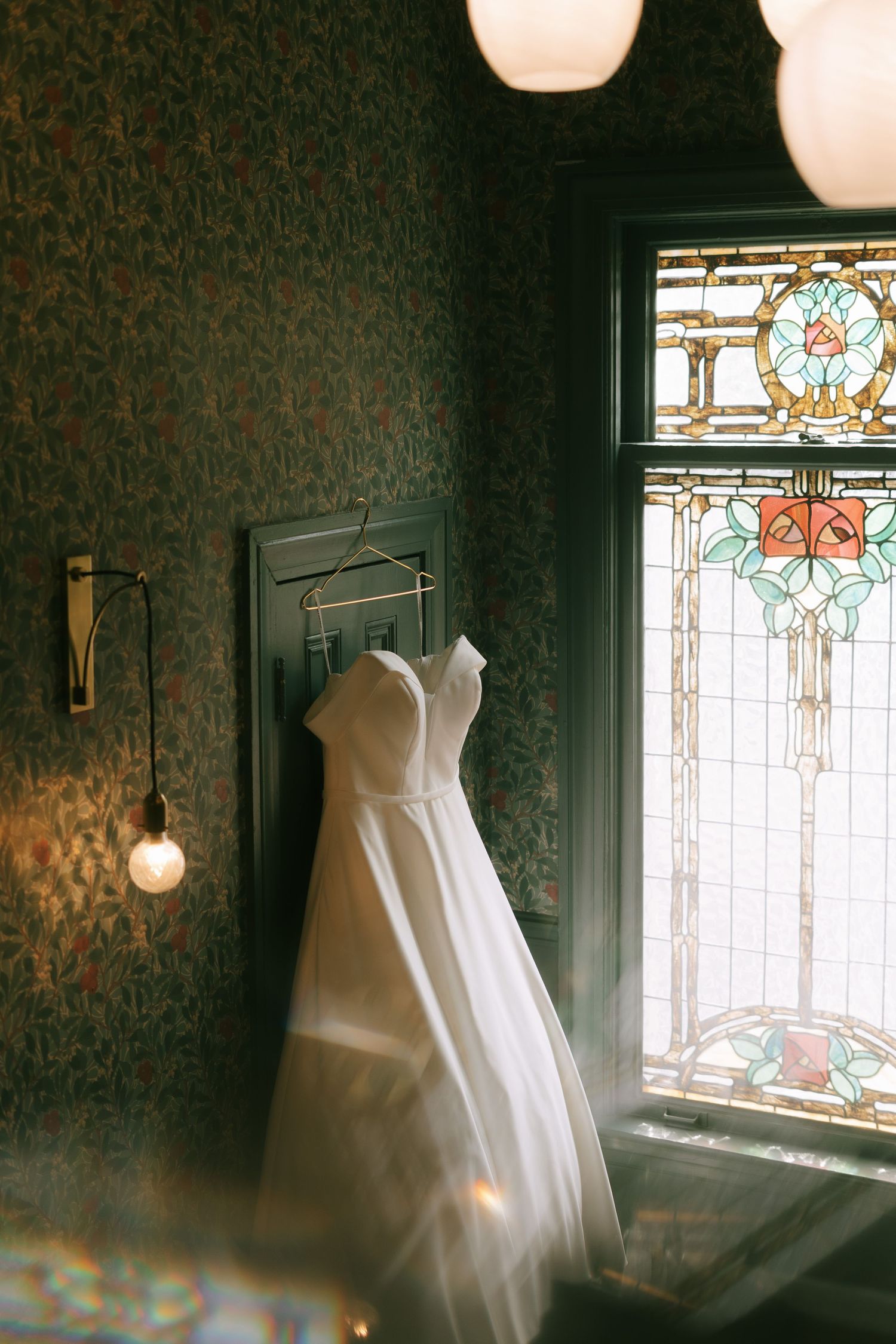 Wedding dress display near ornate stained glass window with natural lighting.