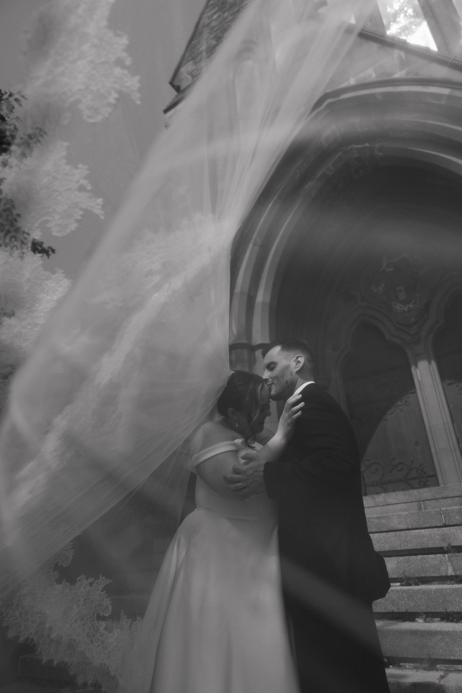 An intimate wedding portrait captured through flowing veil at church entrance.