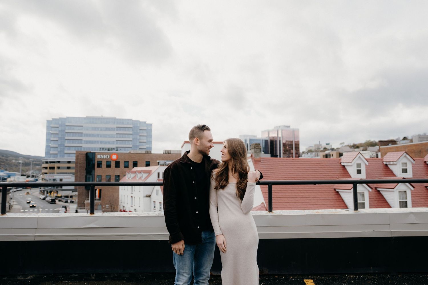 Romantic couple moment captured on urban rooftop with cloudy sky and buildings in view.