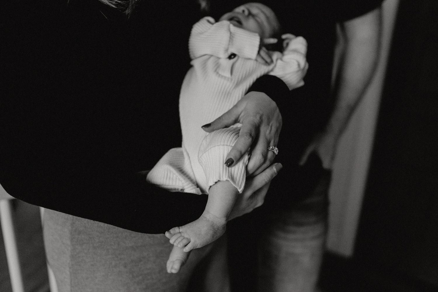 Gentle hands holding and comforting a tiny newborn baby in black and white.