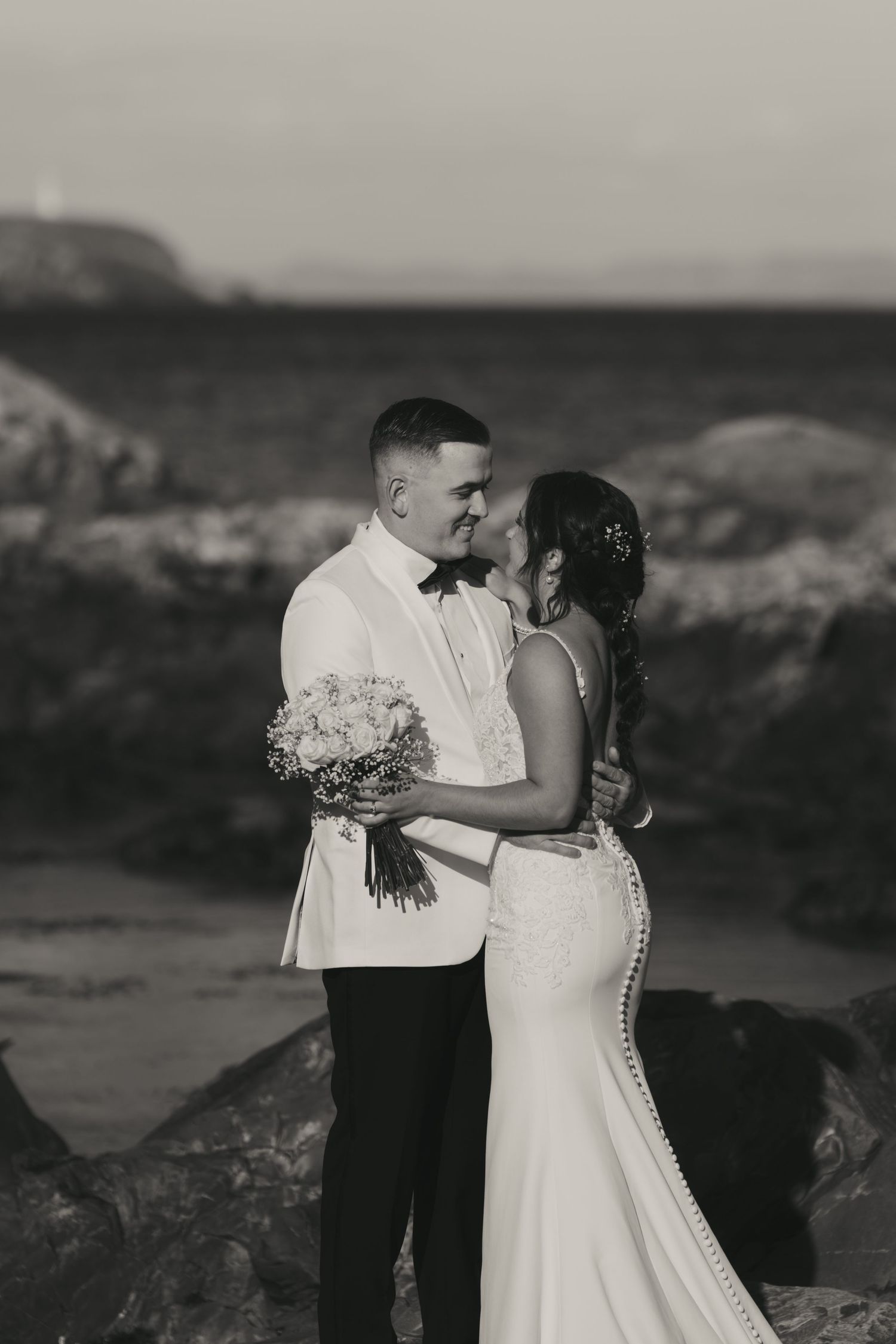 A romantic black and white wedding photo series showing a couple embracing on a scenic mountain overlook.