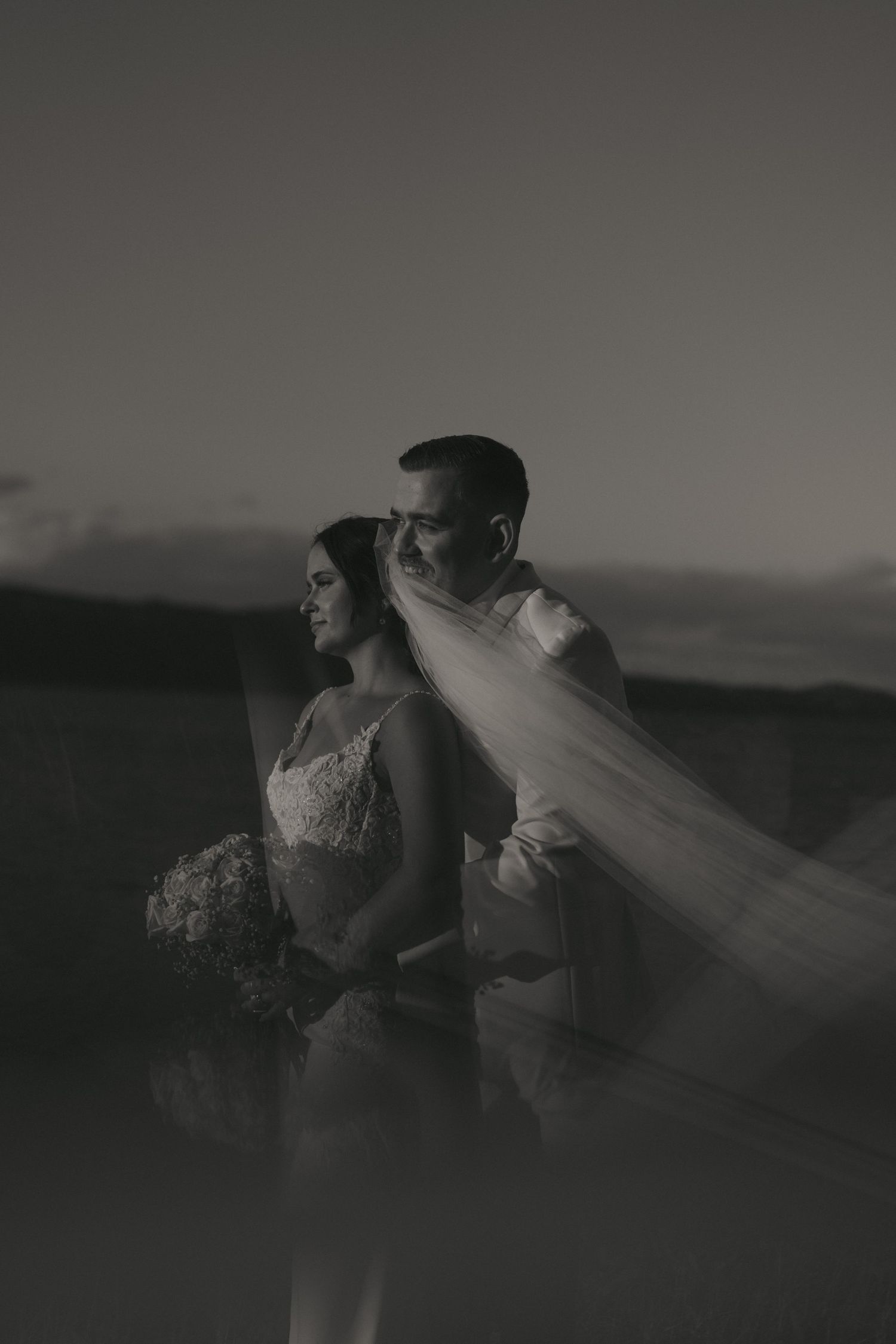 A romantic black and white wedding photo series showing a couple embracing as a veil flows in the wind.