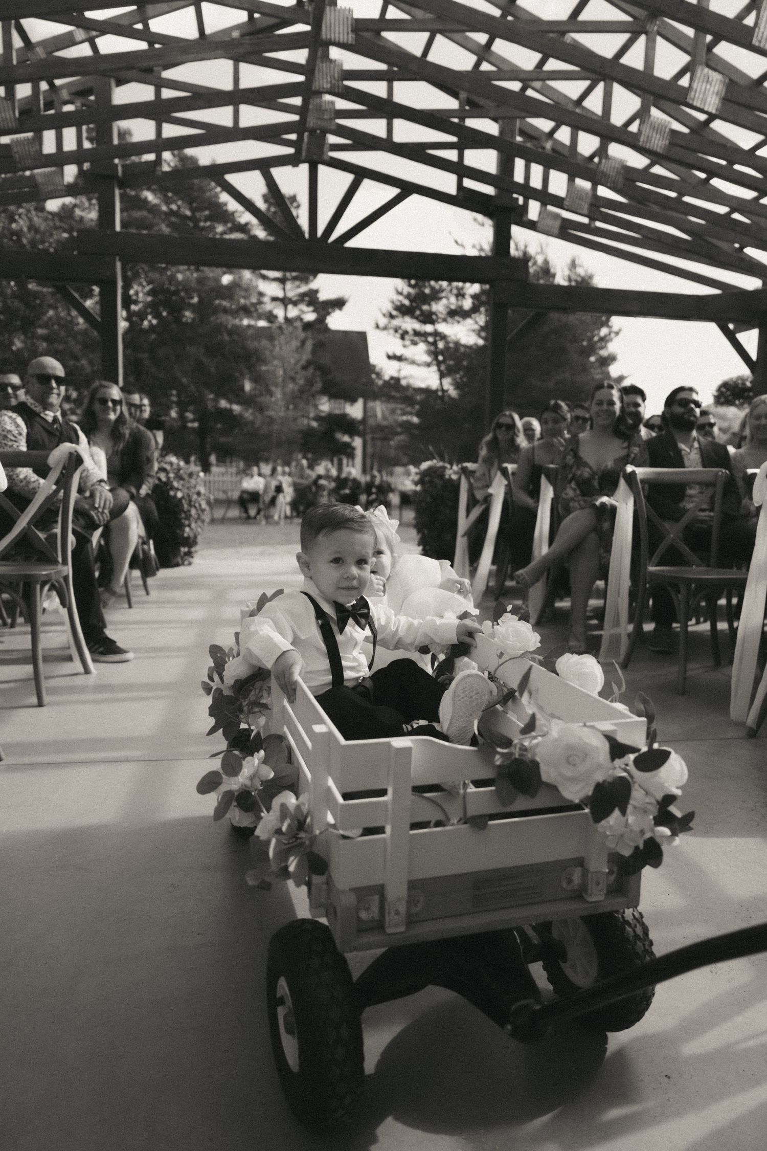 A small decorated wagon carries a young passenger during an outdoor event under a covered pavilion.