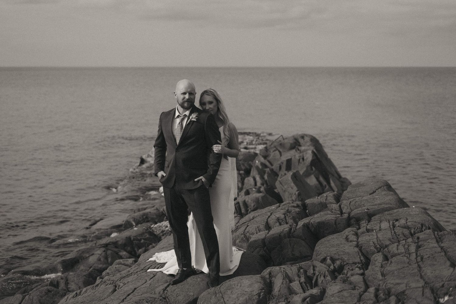 Black and white wedding portrait captured on dramatic rocky coastline.