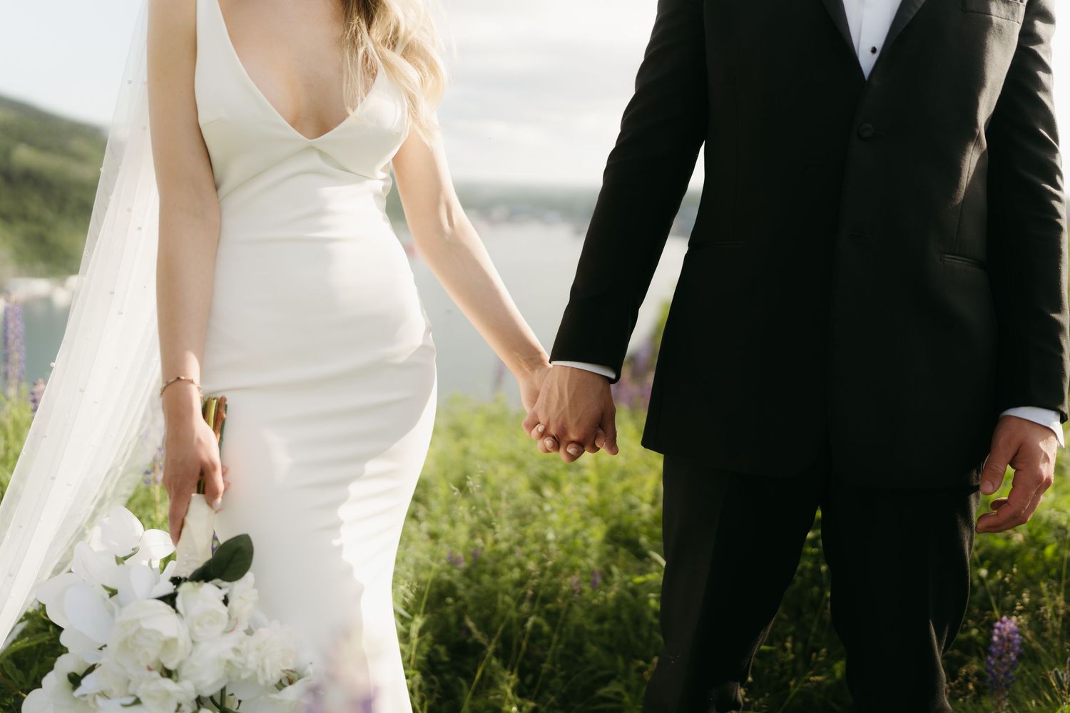 A romantic wedding couple walks through a field of purple lupine flowers by the coast.