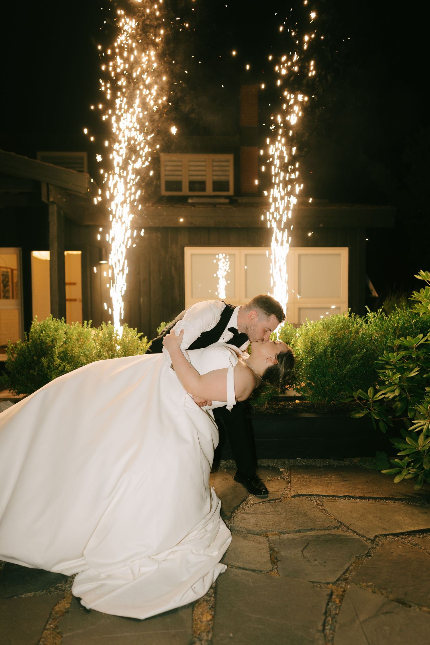 Dramatic dip pose with sparklers illuminating outdoor wedding celebration.