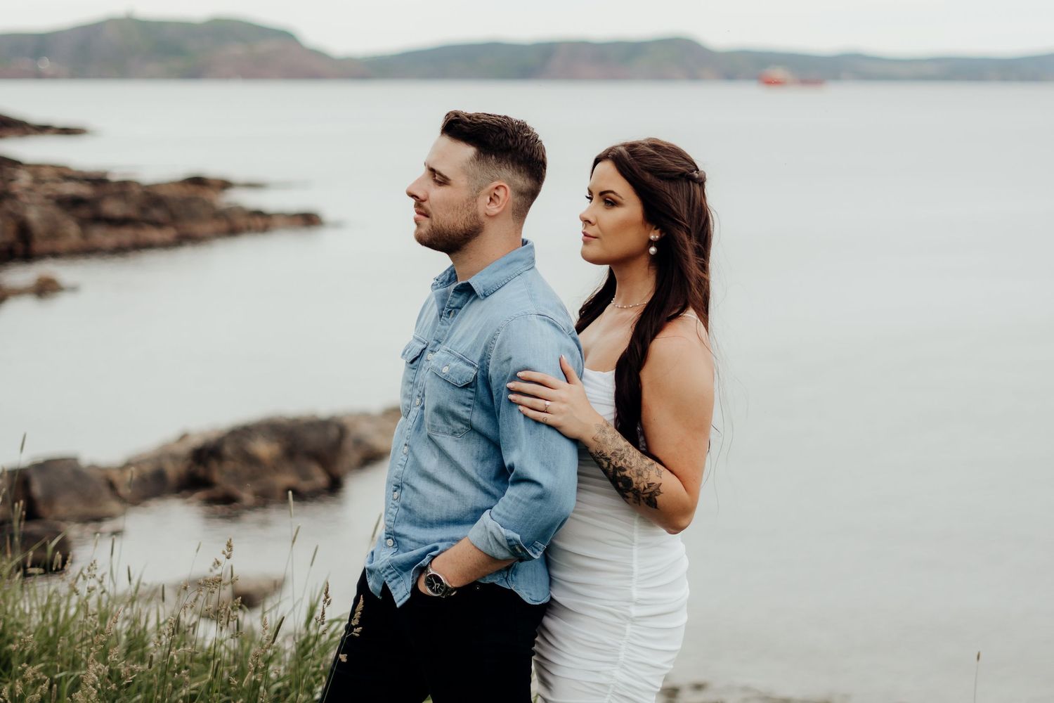 Couple poses together on coastal cliffs overlooking ocean views.