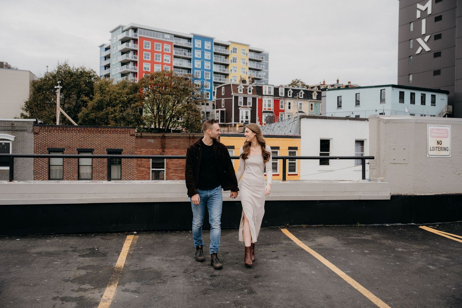 Couple walking through empty parking garage with downtown buildings in background.