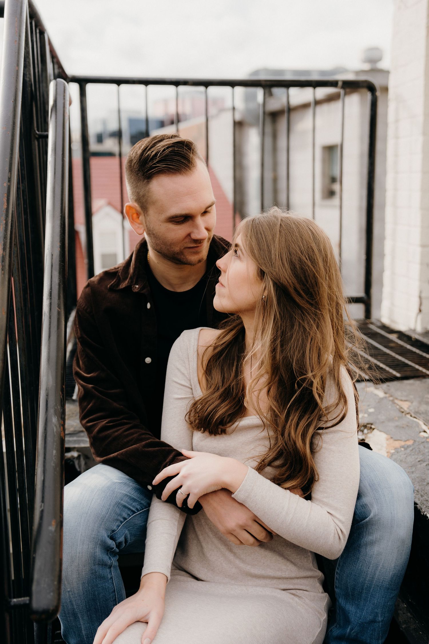 Couple in casual wear sharing romantic moments on urban balcony setting.