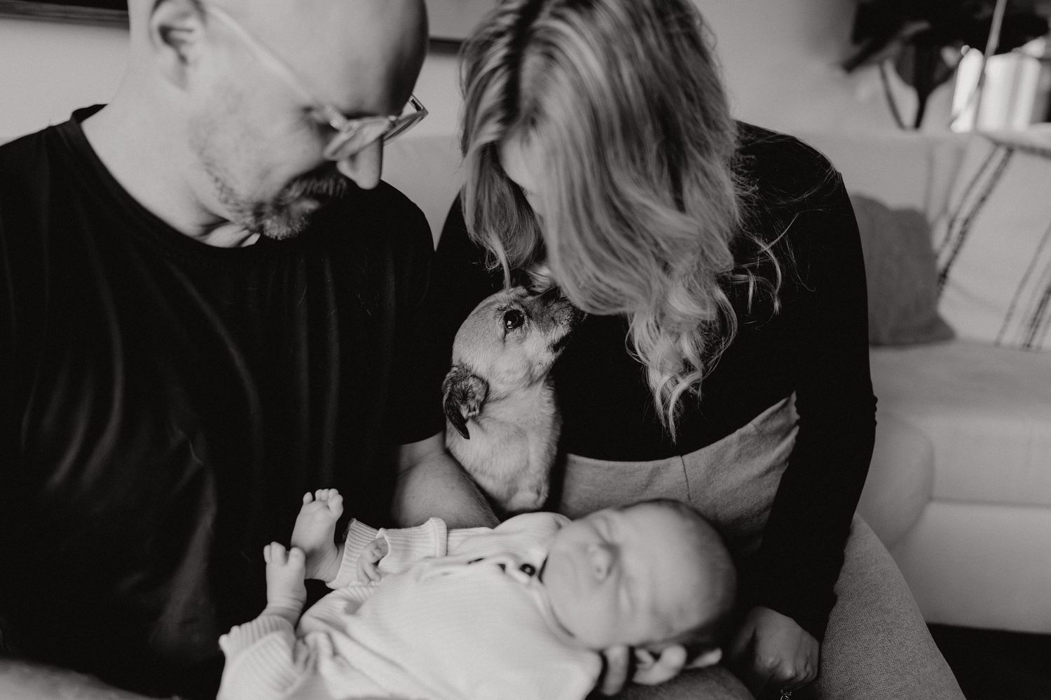 An intimate black and white portrait of parents bonding with their newborn baby on a couch.