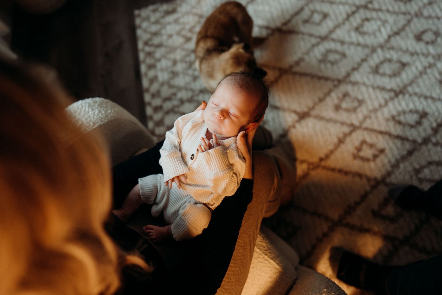 Intimate photograph of baby in white clothing on patterned floor.