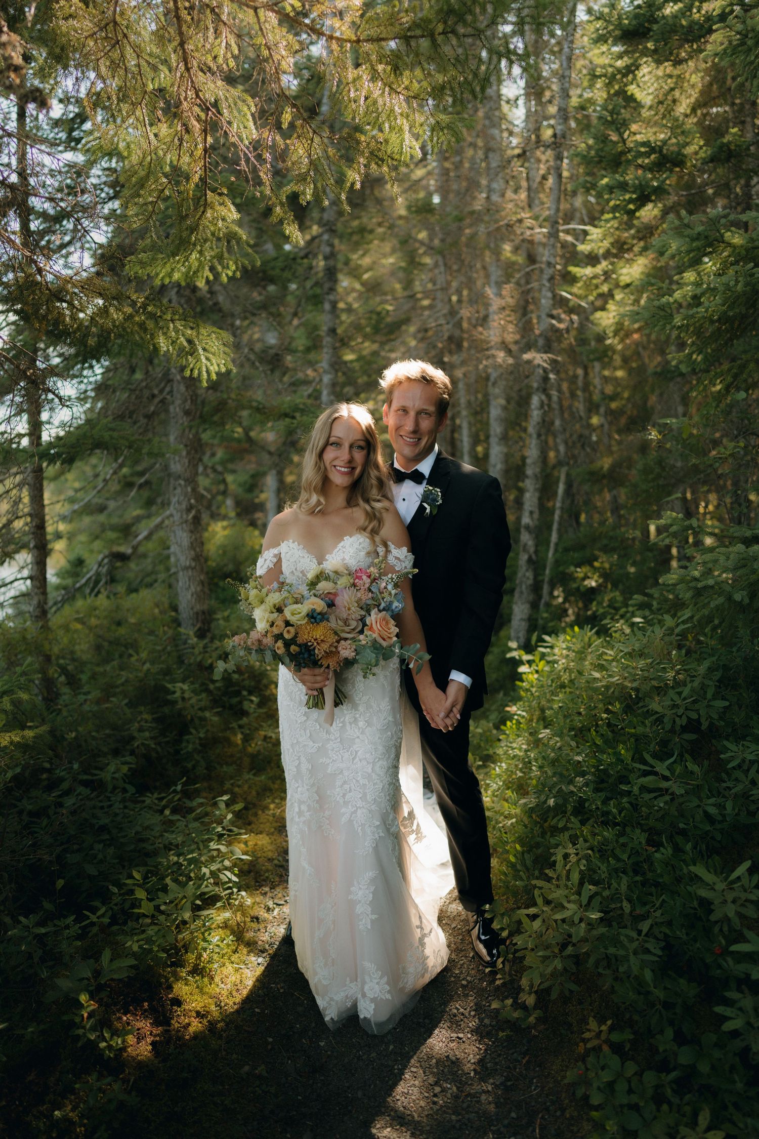 A bride and groom share intimate moments in a lush evergreen forest setting during their wedding photoshoot.