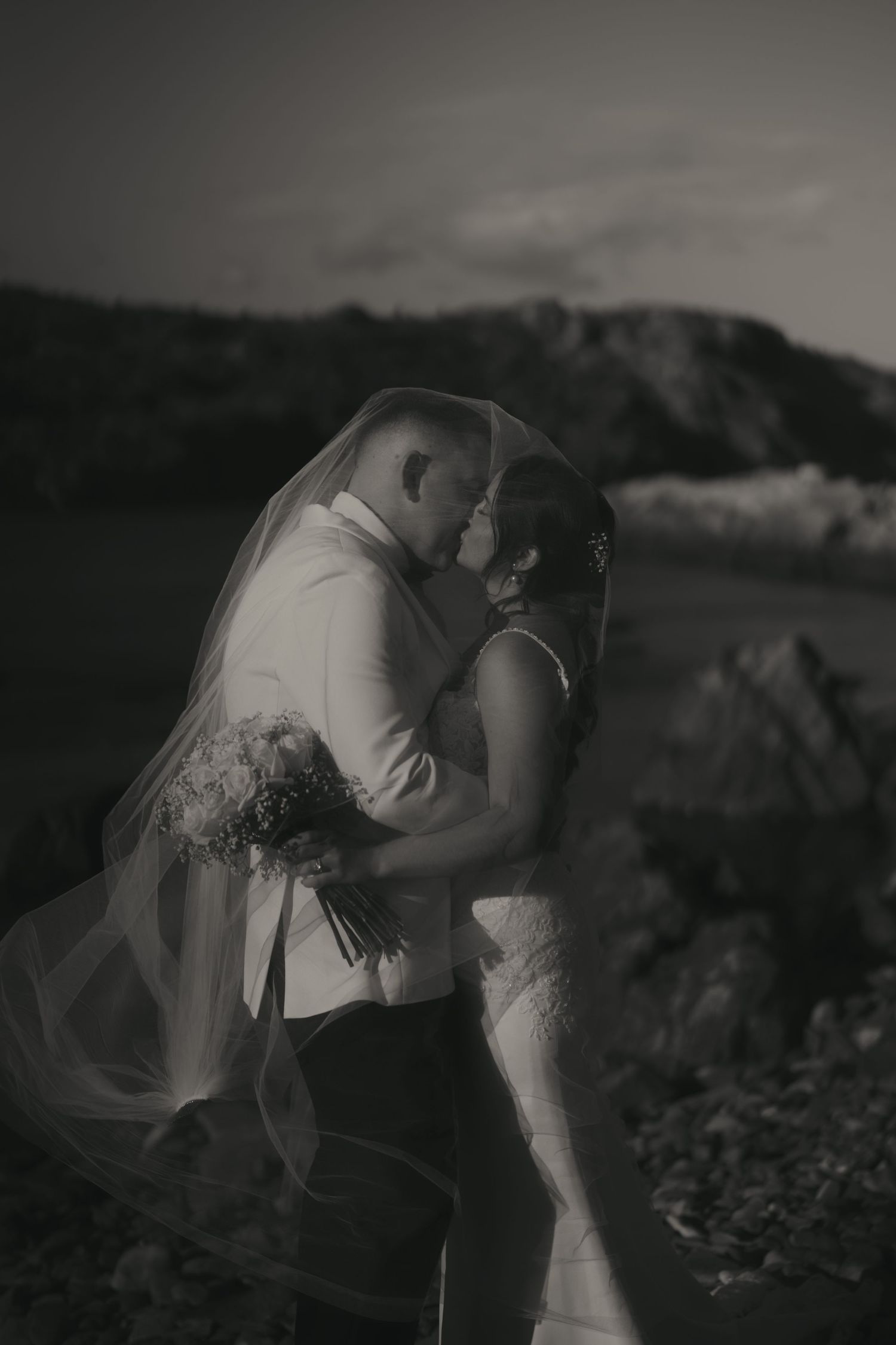 A romantic black and white wedding photo series showing a couple in intimate poses with flowing veil and natural scenery.