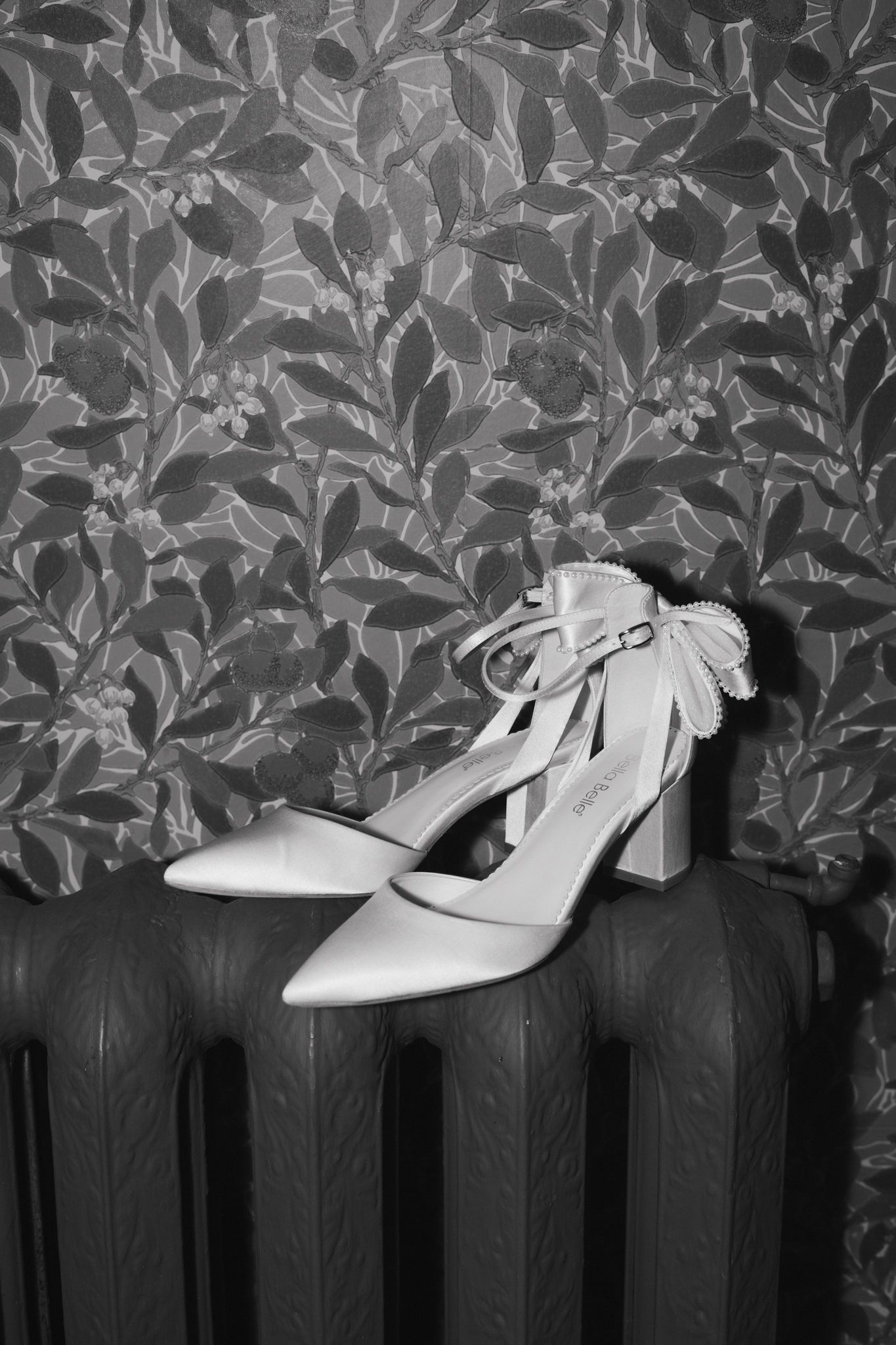 White bridal shoes displayed against floral wallpaper on a vintage radiator.
