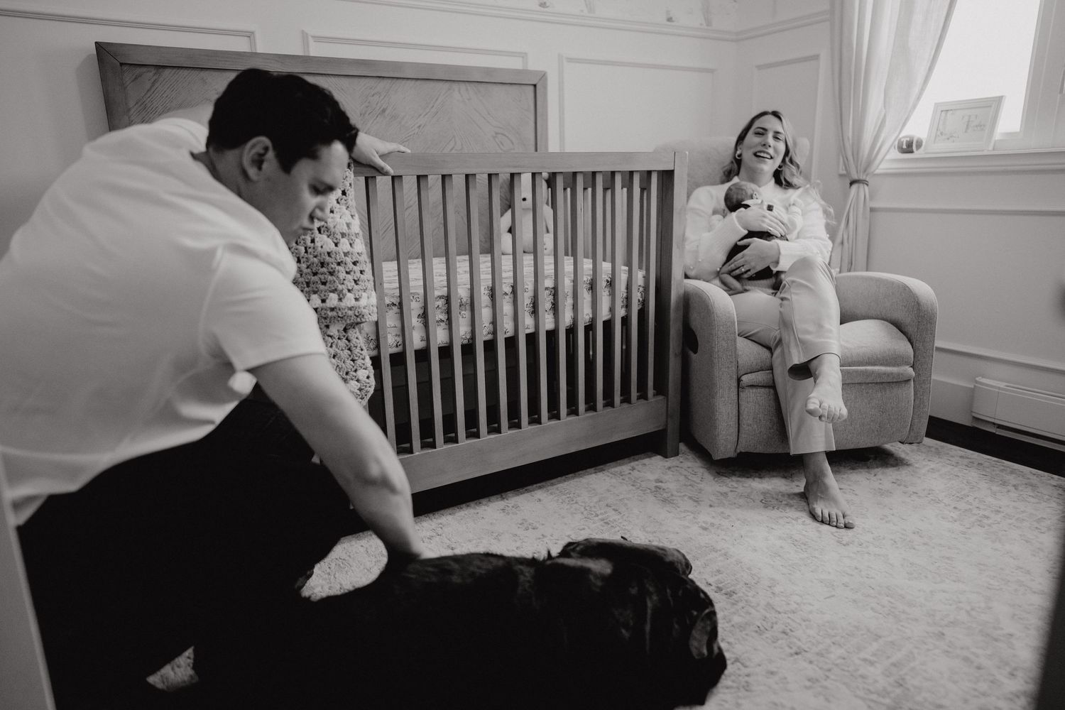 Black and white nursery scene showing a crib and rocking chair in a cozy corner.