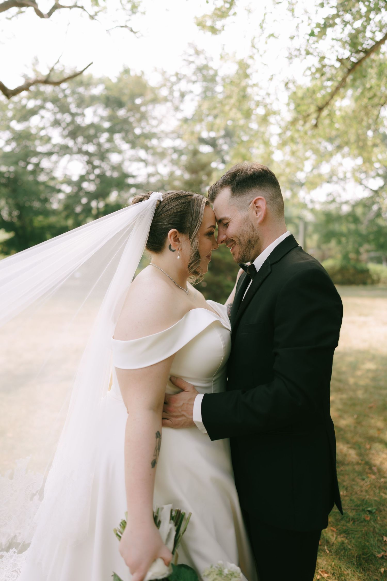 Intimate moment captured between newlyweds with flowing white veil in outdoor setting.