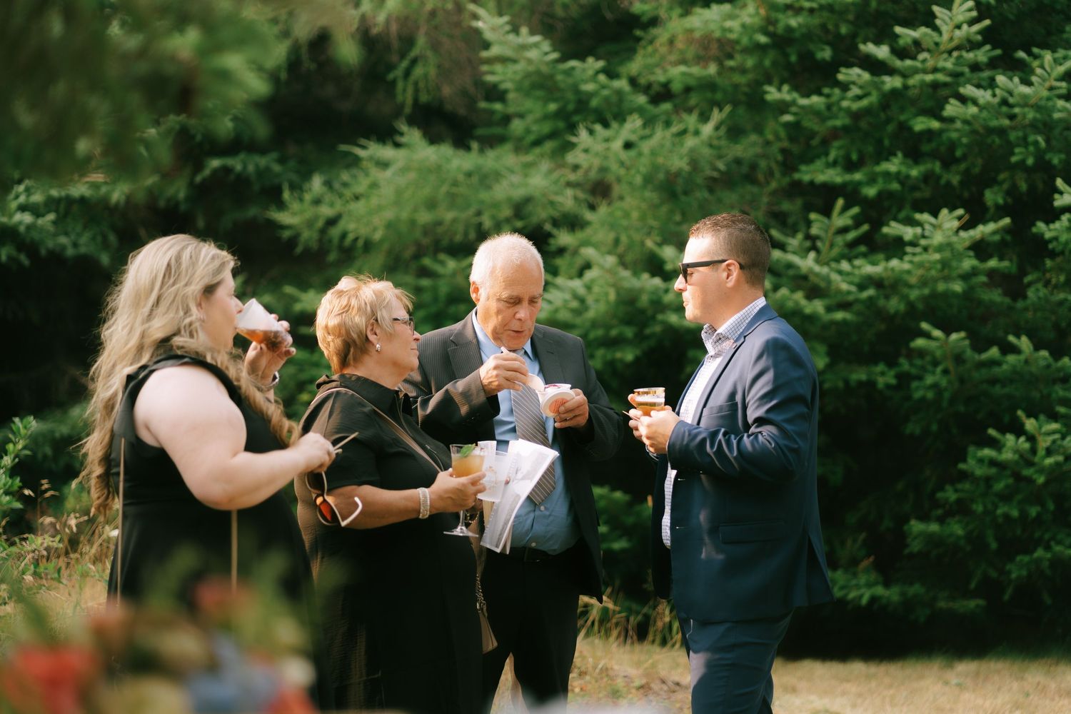 Outdoor celebration with guests enjoying drinks in a natural garden setting.