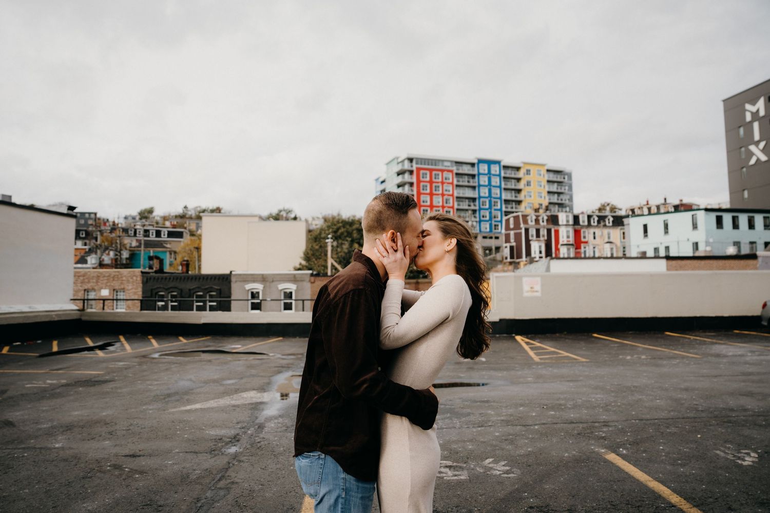 Romantic couple sharing an intimate moment on an urban rooftop with city buildings in the background.